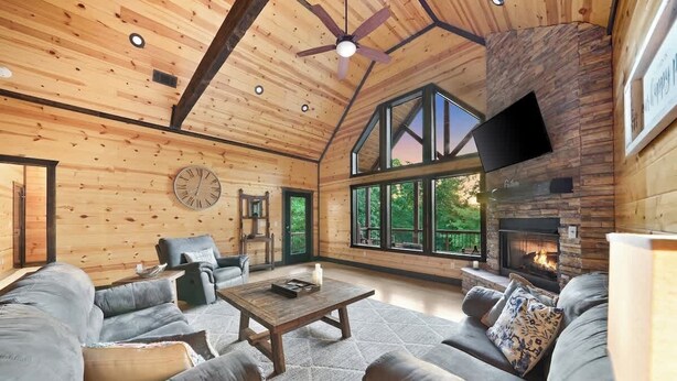 A log cabin interior with a fireplace, leather sofas, a wooden coffee table, and large windows. - 3 King Suites, Hot Tub, Firepit, Playset, Dogs OK (Broken Bow)