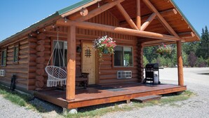 A log cabin with a porch, a hanging chair, and a grill.