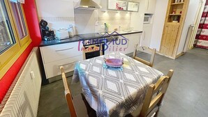 A compact kitchen with white cabinets, a stainless steel range hood, and a small dining area with a checkered tablecloth.