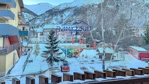 A snow-covered outdoor area with a playground, a building with balconies, and a mountain backdrop.