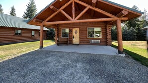 A log cabin with a covered porch, a front door, and a bench.