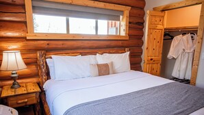A wooden cabin bedroom with a bed, a nightstand, a lamp, and a window.