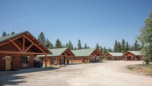 A row of log cabins with green roofs, arranged in a row along a gravel driveway.