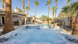 A hot tub surrounded by palm trees and a pool, with a stone wall and a building in the background. - Oasis in the Desert w/ Heated Pool Fully Renovated (North Las Vegas)