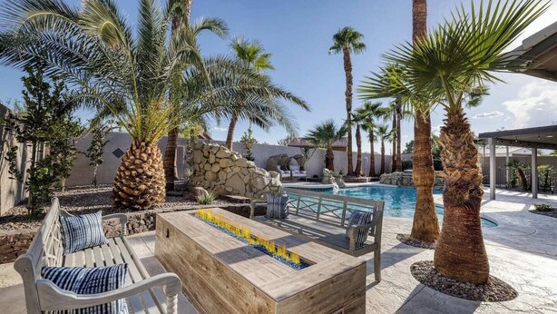 A poolside area with a wooden fire pit, seating, and palm trees. - Oasis in the Desert w/ Heated Pool Fully Renovated (North Las Vegas)