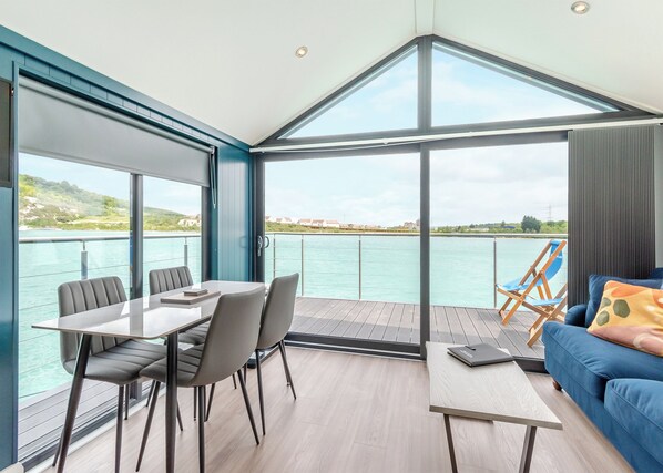 A modern room with a dining table, chairs, a sofa, and a view of the water.