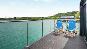 Een terras met twee blauwe loungestoelen, een leuning en uitzicht op een rustig waterlichaam.