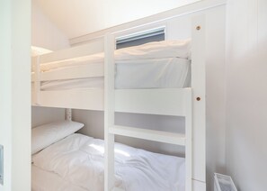 Quarto com beliche, roupa de cama branca, janela com persianas e porta com tranca.