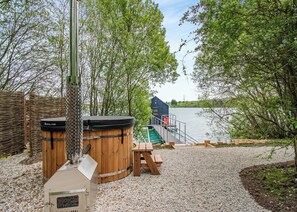 Une terrasse en bois avec un barbecue, un petit quai et un bateau.