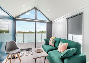 A modern room with a green sofa, a chair, and a table. It has a large window with a view of the water and a building in the distance. - 1 bedroom accommodation in Halling (Halling)