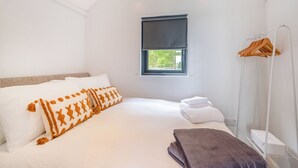 A bedroom with a bed, pillows, a window, a towel rack, and a box on the nightstand.