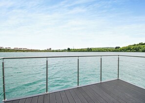 Une terrasse en bois avec une rambarde en métal donnant sur une étendue d’eau.
