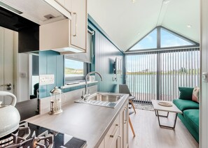 A modern kitchen with a large island, a dining area with a green sofa, and a view of the water through large windows. - 1 bedroom accommodation in Halling (Halling)