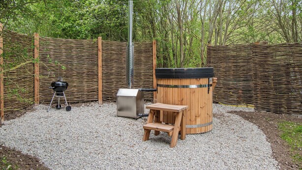 A backyard with a barbecue grill, a wooden barrel, and a wooden bench.
