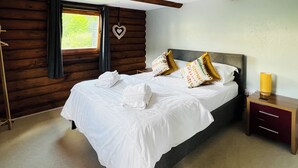 Un dormitorio con una cama grande, cabecera de madera, una mesita de noche con lámpara y una ventana con cortinas.