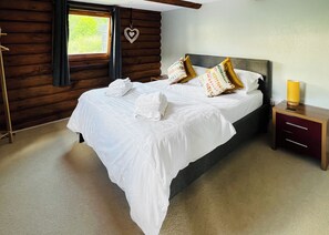 Une chambre à coucher avec un grand lit, une tête de lit en bois, une table de chevet avec une lampe et une fenêtre avec des rideaux.