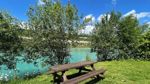 Una mesa de picnic junto a un lago, con árboles y césped.