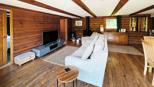 Interior de una cabaña de troncos con sofá, televisión, piso de madera y zona de comedor.