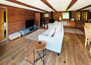 L’intérieur d’une cabane en rondins, avec un canapé, un téléviseur, un plancher en bois et un coin repas.