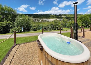 A hot tub with a wooden deck, surrounded by a rope barrier and a metal fence, with a scenic view of a road and greenery in the background. - 1 bedroom accommodation in Halling (Halling)