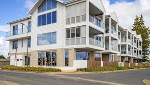 A modern multi-story residential building with balconies, large windows, and a landscaped front yard. - Moana Beach, Seafront Apartment (Moana)