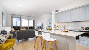 A modern kitchen with a central island, grey cabinets, and wooden stools. - Moana Beach, Seafront Apartment (Moana)