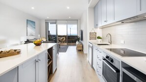 A modern kitchen with white cabinets, a large island, and a view to a balcony. - Moana Beach, Seafront Apartment (Moana)