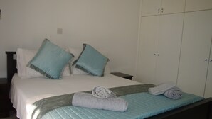 A neatly made bed with a blue quilt, two pillows, and two rolled towels on a dark headboard.