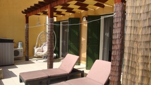 A covered outdoor seating area with two lounge chairs and a hanging chair.