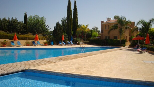 A swimming pool with lounge chairs and umbrellas, surrounded by trees and a building.
