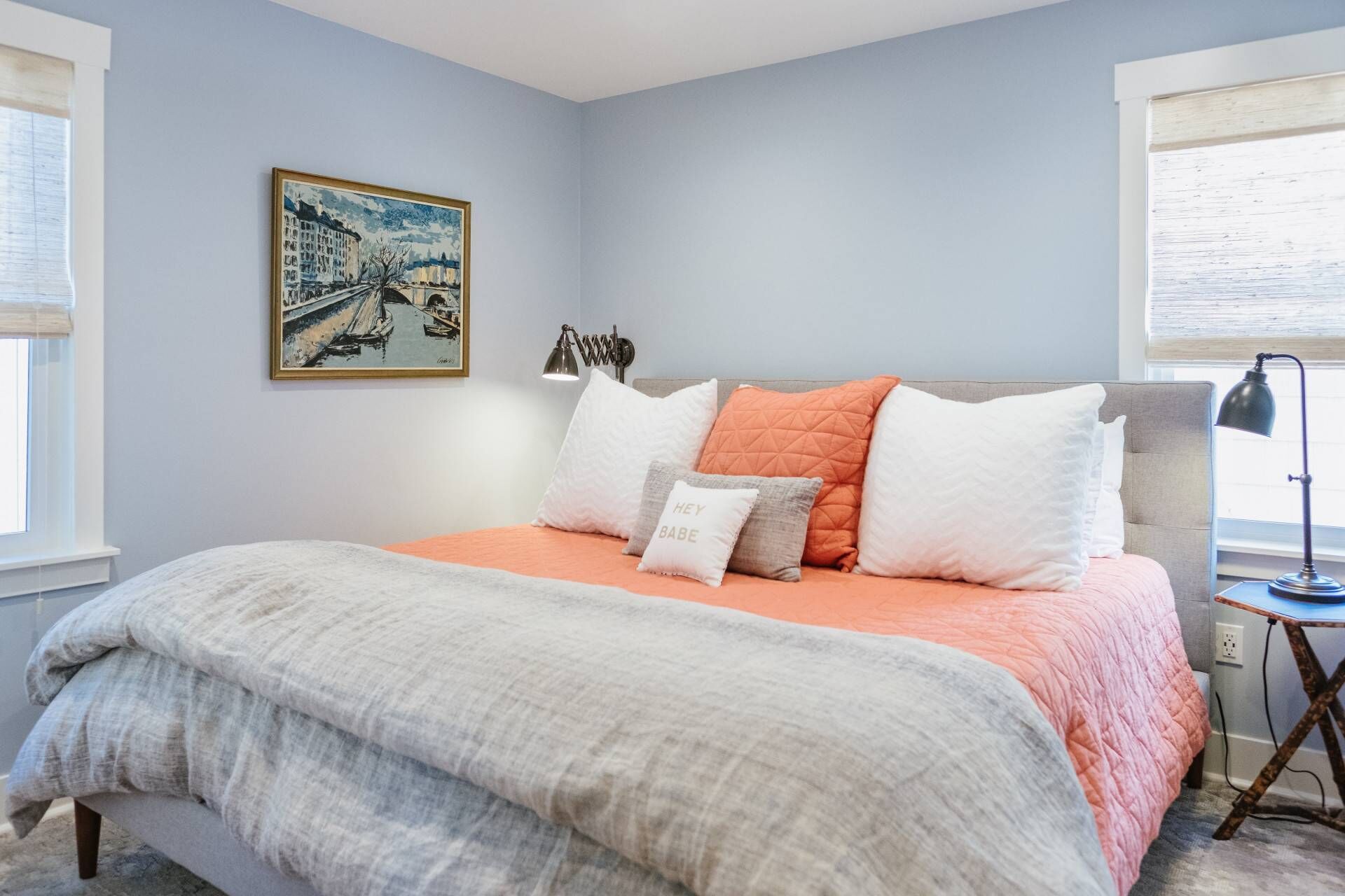 A bedroom with a bed, pillows, a lamp, and a painting on the wall.