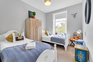 A bedroom with two beds, a wooden wardrobe, a window with a view, and a small table with a lamp. - Poets Apartment By My Getaways (Worthing)