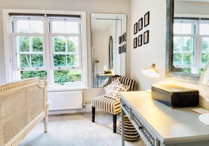 A room with a rattan chair, a striped sofa, a table with a lamp, and a mirror on the wall. - Poets Apartment By My Getaways (Worthing)