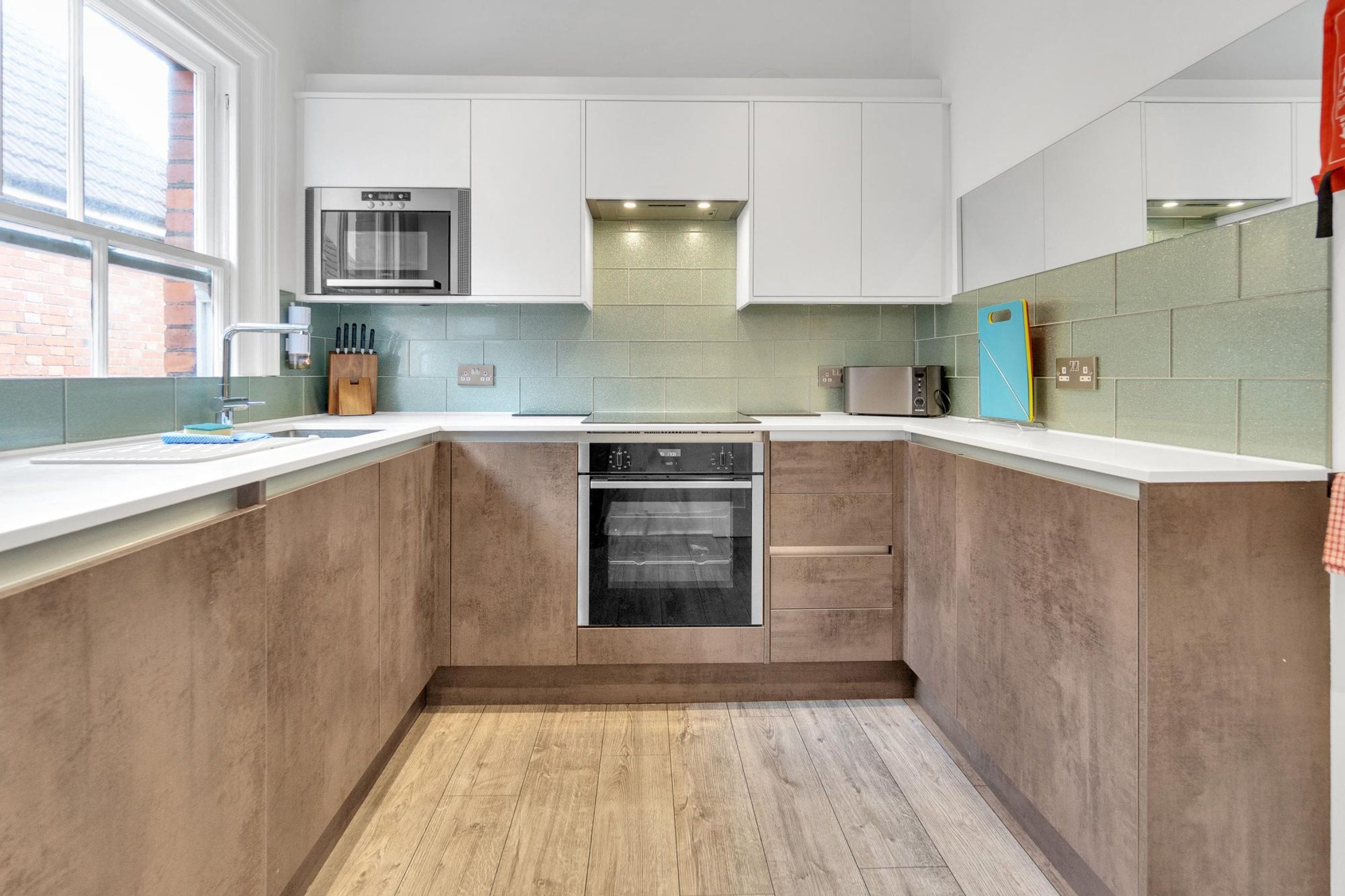 A modern kitchen with white cabinets, a built-in oven, and a window providing natural light.