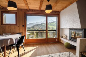 Een houten interieur met een eettafel, stoelen, een open haard en een balkon met uitzicht op de bergen.