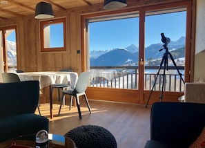 Quarto com decoração em madeira, varanda com telescópio e vista para montanhas e um lago.