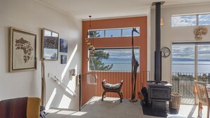 A cozy living room with a view of the sea, a fireplace, and a staircase leading to an upper level.
