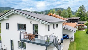 Une maison moderne à deux étages, dotée d’un balcon, d’un petit garage attenant et d’une voiture garée à l’intérieur.
