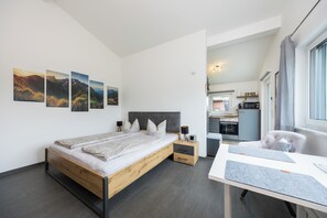 A modern bedroom with a wooden bed, a desk, and a view of the kitchen. - 25-square-meter apartment with a balcony and a separate bedroom (Bad Feilnbach)