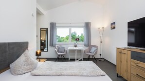 Une chambre moderne comprenant un lit, un bureau, deux chaises, un téléviseur et une fenêtre avec des rideaux.
