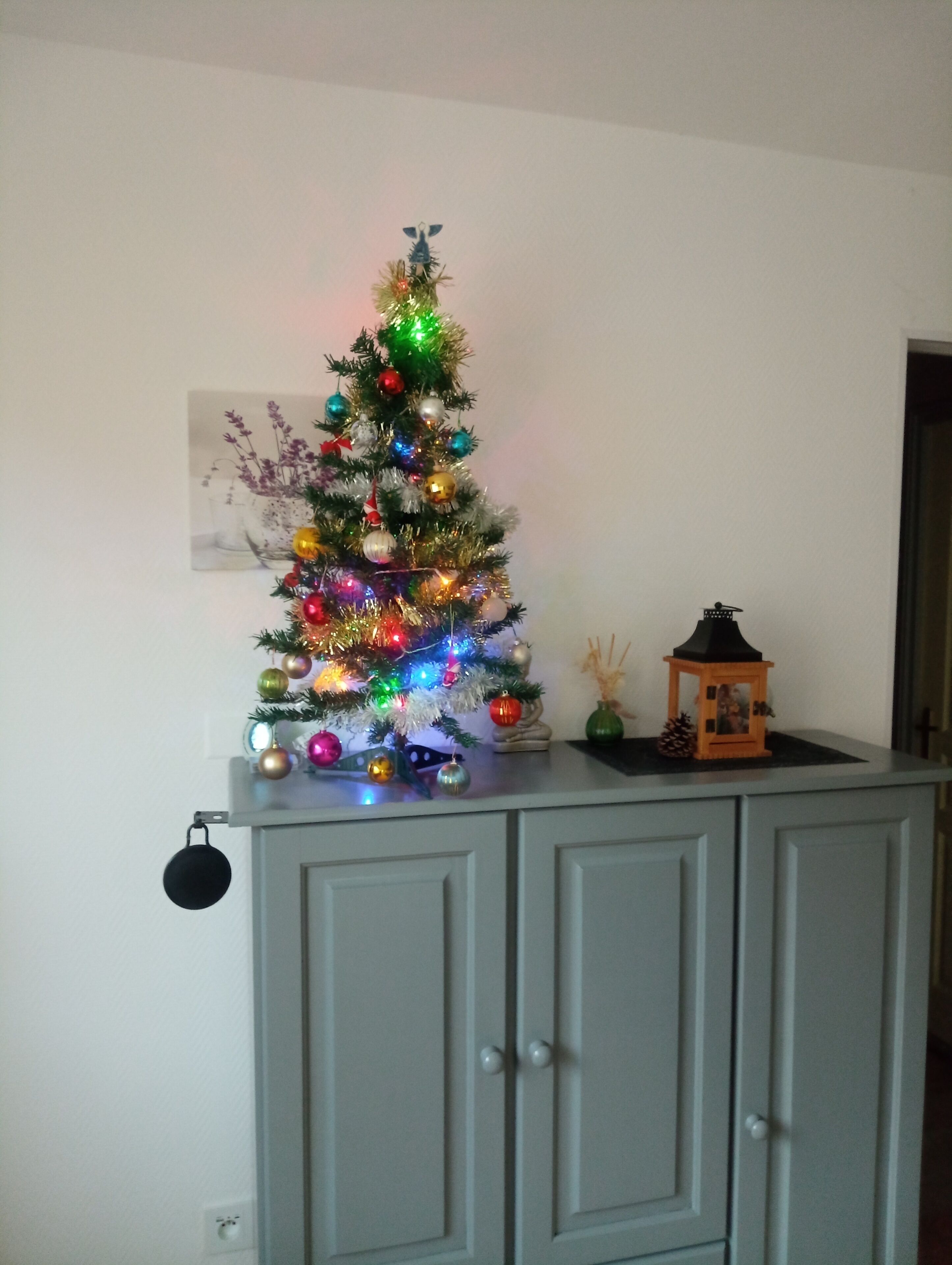 Een versierde kerstboom met kleurrijke versieringen en lichtjes op een kast.