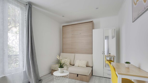 A modern, compact room with a bed, a small round table, a yellow chair, and a window with sheer curtains. - Chic studio near Paris (Colombes)