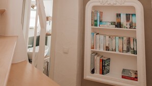 Eine Treppe führt zu einer zweiten Etage mit weißer Reling, einem weißen Bücherregal mit Büchern und einem Ausblick ins Freie durch ein Fenster.