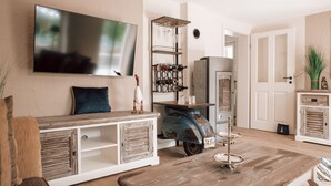 Ein Wohnzimmer mit an der Wand montiertem Fernseher, einem Vintage-Roller, einem Weinkühlschrank und einem Couchtisch aus Holz.