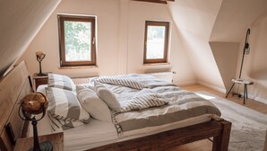 Ein Schlafzimmer mit einem hölzernen Bett, zwei Fenstern, einer Heizung und einer Lampe auf einem Holztisch.
