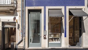 A storefront with a blue-tiled facade, two glass doors with signage reading "STONE BY STONE," and a small outdoor seating area. - PATIO DE FLORES - Beautiful apartment with patio located in downtown Porto (Porto)