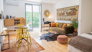 A modern living room with a sofa, a coffee table, a dining area with chairs, and a large window. - PATIO DE FLORES - Beautiful apartment with patio located in downtown Porto (Porto)