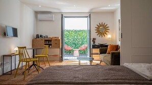 A modern bedroom with a large bed, a desk with chairs, a television, and a balcony with a view of greenery. - PATIO DE FLORES - Beautiful apartment with patio located in downtown Porto (Porto)
