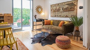 A modern living room with a sofa, coffee table, and chairs. There is a large painting on the wall, a potted plant, and a glass door leading to a balcony. - PATIO DE FLORES - Beautiful apartment with patio located in downtown Porto (Porto)