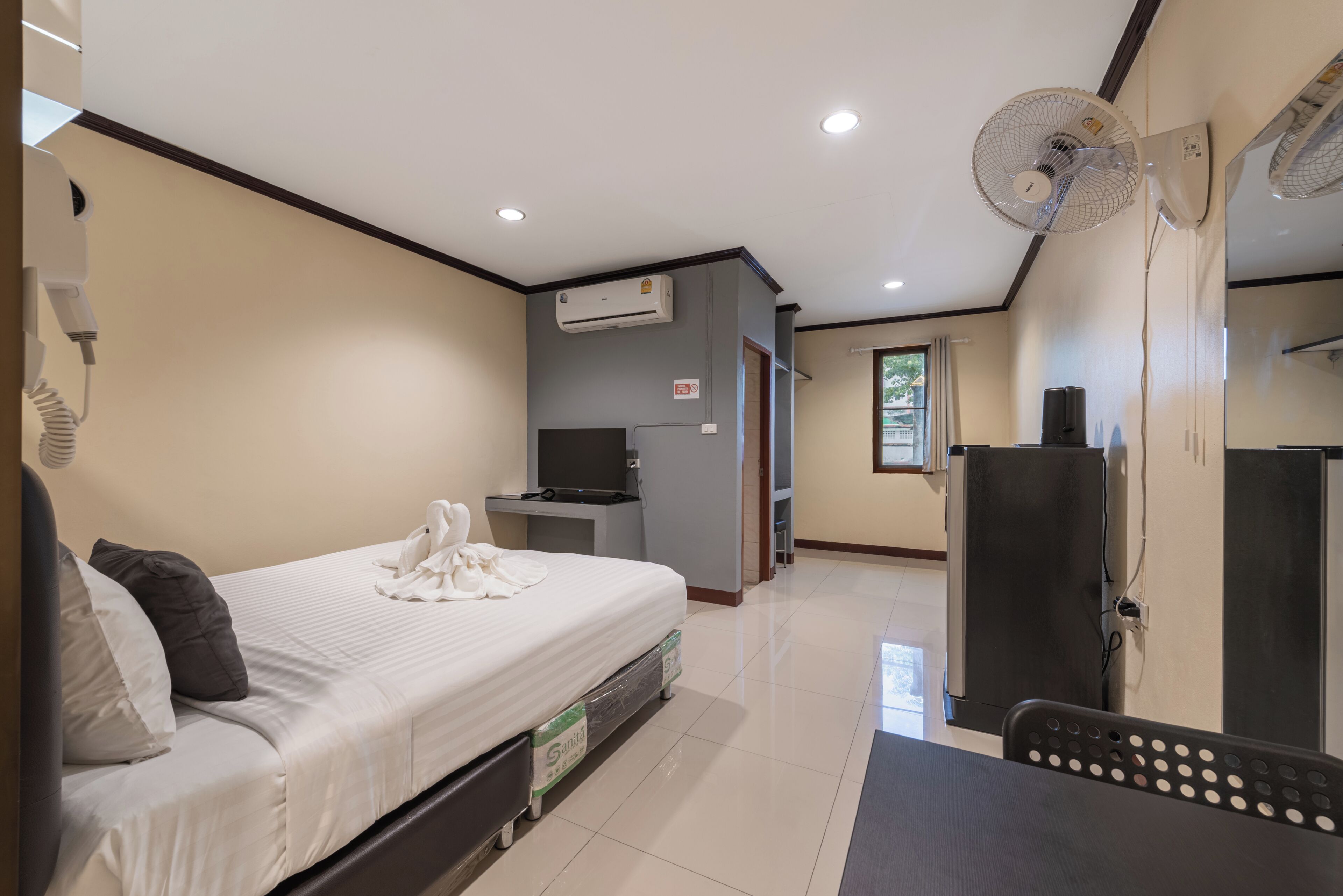 A bedroom with a bed, a desk, an air conditioner, a TV, and a refrigerator.